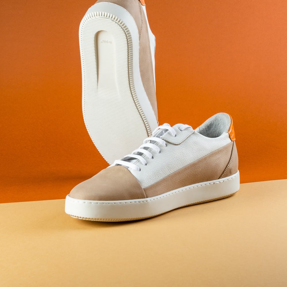 stylish white and brown pair of  sneaker one place on top of two white smooth stones and twig on the side place on orange surface