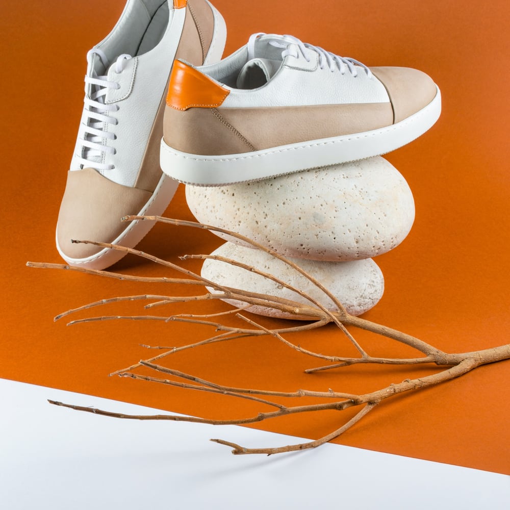 stylish white and brown pair of  sneaker one place on top of two white smooth stones and twig on the side place on orange surface 