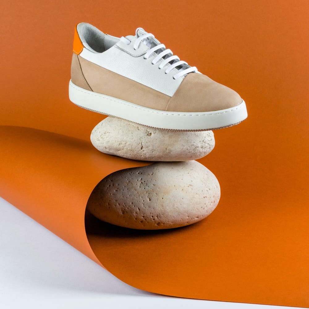 stylish white and brown sneaker  place on top of two white smooth stones on orange surface