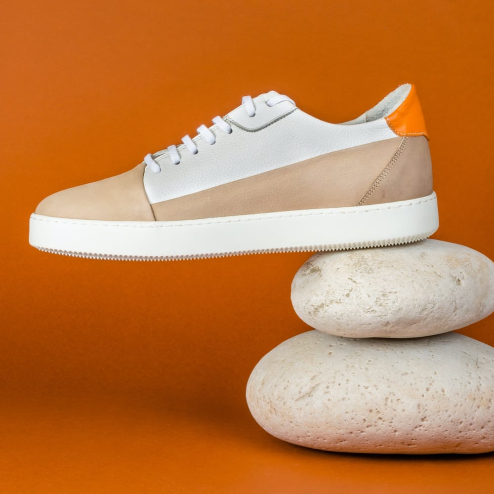 stylish white and brown sneaker ,  resting over two white smooth stones on the heels on orange surface